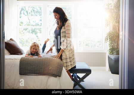 Donna felice e incinta e gioca con il bambino a letto per amore, nutrire i genitori e legarsi insieme. Ritratto, madre e bambino per divertimento giocoso, emozionale Foto Stock