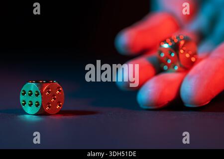 La mano lancia i dadi su uno sfondo scuro con una messa a fuoco selettiva. Foto Stock
