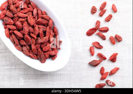 Bacche di goji, frutta secca in ciotola bianca su lino. Anche wolfberry cinese, medlar rosso e vite matrimoniale. Frutta dolce, rossa-arancia brillante. Foto Stock