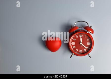 Cuore rosso e sveglia nera su abbinamento simbolico blu che suggerisce la connessione dell'amore con il tempo, l'urgenza o la presenza emotiva duratura. Foto Stock