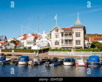 Piccole imbarcazioni ormeggiate lungo la banchina del porto con la storica villa in legno di Hamngatan a Marstrand, Bohuslän, costa occidentale della Svezia Foto Stock
