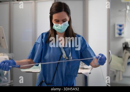 Un infermiere dedicato in una moderna UTI, che indossa scrub protettivi e una maschera facciale, esemplificando l'impegno degli operatori sanitari in prima linea nell'assistenza ai pazienti Foto Stock
