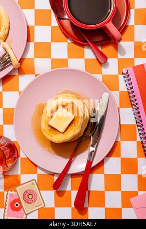 Una deliziosa colazione a base di pancake preparata su un piatto rosa con burro e sciroppo, accompagnata da caffè in una tazza rossa. Luminoso e allegro, perfetto per una ragazza Foto Stock