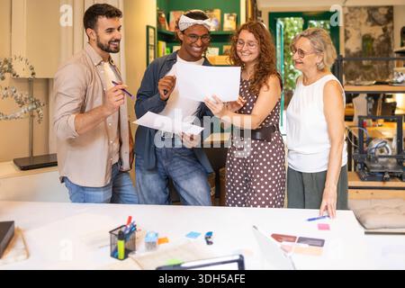 Un gruppo eterogeneo di colleghi impegnato in una discussione vivace, condividendo idee e collaborando in uno spazio di coworking luminoso e moderno, promuovendo la creatività Foto Stock