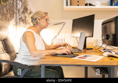 Una donna professionista anziana che lavora su un notebook a una scrivania di legno in un moderno ambiente di ufficio. L'area di lavoro pulita favorisce la concentrazione e la produttività d Foto Stock