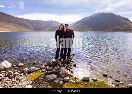 Due escursionisti si godranno un'avventura mozzafiato all'alba in una laguna di montagna incontaminata, circondata da aspre cime e cieli azzurri cristallini, catturando l'ess Foto Stock