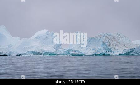 Accattivante immagine di iceberg torreggianti che fluttuano serenamente nelle fredde acque della Groenlandia, mostrando le loro impressionanti texture e la dura bellezza di Foto Stock