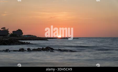 Un vivace tramonto dipinge la spiaggia dei Caraibi in tonalità calde. Il sole tramonta sulle acque calme, creando un'atmosfera serena con sagome di rocce e dist Foto Stock