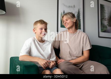 Una madre e un figlio gioiosi condividono un momento di risate e connessione mentre si siedono insieme su un accogliente divano verde in un bellissimo arredamento e pieno di luce Foto Stock
