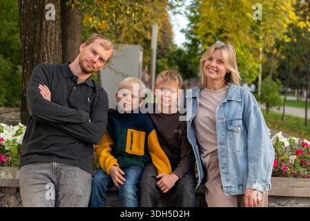 Una famiglia gioiosa che si diverte a fare una piacevole passeggiata in uno splendido parco. La madre e il padre sorridono con i loro due figli, circondati da una vegetazione lussureggiante e. Foto Stock
