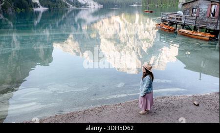 Una donna è affascinata dallo splendido scenario del Lago di Braies, Pragser Wildsee, con maestose montagne che si riflettono sul tranquillo lago, catturando Foto Stock