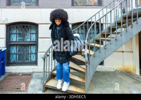 Donna nera felice in piedi su scale di metallo a New york Foto Stock