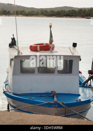 Barca a motore ormeggiata al molo di Porto San Paolo, in Sardegna con anello salvavita e bandiera italiana, primo piano verticale Foto Stock