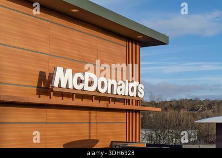 Vista all'aperto su un cartello del ristorante britannico McDonald's e su un edificio in un parco al dettaglio con luce solare intensa. Foto Stock