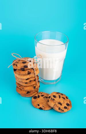 Bicchiere di latte fresco e biscotti scuri a base di cioccolato su sfondo blu Foto Stock