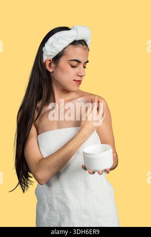Giovane donna che applica crema idratante sulle spalle per la cura e il benessere del corpo Foto Stock