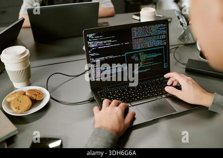 Giovane uomo caucasico adulto che scrive codice su laptop mentre lavora in ufficio Foto Stock