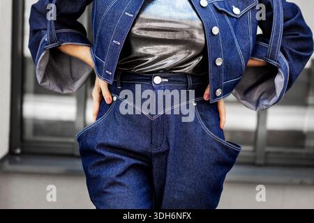 Donna elegante che indossa giacca e pantaloni in denim con tasche grandi e maniche larghe. Moda di strada alla moda, elegante modella femminile in posa all'aperto Foto Stock