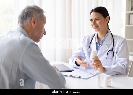 Medico donna che consulta un paziente di sesso maschile anziano presso il banco della clinica, che spiega i farmaci Foto Stock
