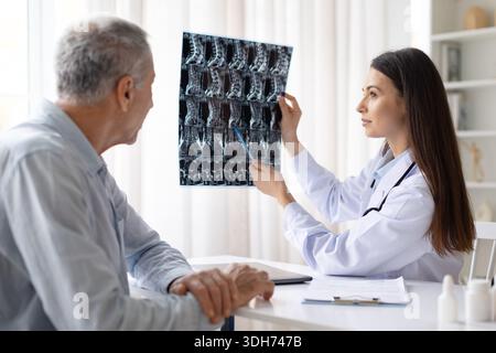 Medico donna che spiega l'immagine a raggi x spinali al paziente di sesso maschile durante la consultazione medica Foto Stock