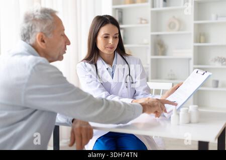 Medico donna che esamina il documento medico con paziente di sesso maschile anziano durante la consultazione Foto Stock