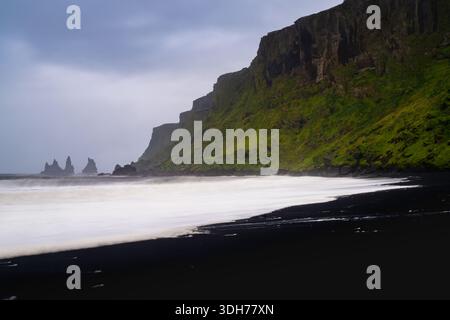 Una vista della spiaggia di sabbia nera di Vikurfjara con i faraglioni di mare di Reynisdrangar in lontananza all'alba Foto Stock