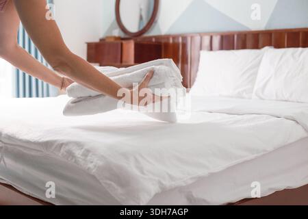 Le mani posizionano una pila di asciugamani bianchi piegati su un letto ben fatto in una camera d'albergo o in una pensione. Pulizia delle camere dell'hotel. Foto Stock