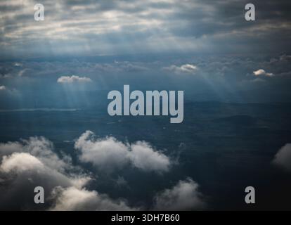 Una vista aerea cattura spettacolari nuvole illuminate da raggi di luce del sole che penetrano attraverso la fitta copertura di nuvole grigie sulle colline ondulate e vall Foto Stock