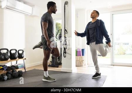 Diversi partner di allenamento maschile che si allungano e si bilanciano su una gamba nella palestra domestica con i kettlebell Foto Stock