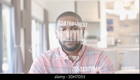 Uomo seduto che indossa una camicia a quadri rosa in una luminosa zona soggiorno cucina, con sovrapposizioni numeriche bianche Foto Stock