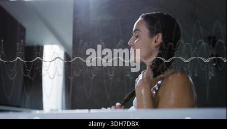 Tenendo una treccia bagnata, una donna adulta in un asciugamano seduto nella vasca da bagno vicino alla finestra con la forma d'onda, spazio di copia Foto Stock