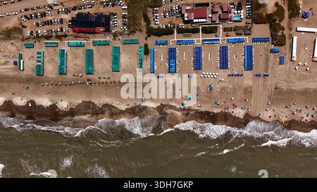 Vista aerea dall'alto verso il basso di una spiaggia affollata a Pinamar, Argentina, caratterizzata da tende colorate e onde oceaniche. Foto Stock