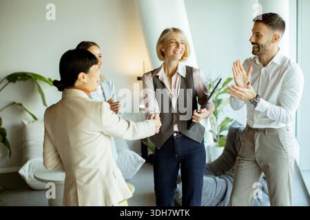 Un gruppo di quattro persone si trova in un ufficio. Stanno sorridendo e interagendo tra loro. Due tengono le bevande mentre stringono la mano. Sembra essere un Foto Stock