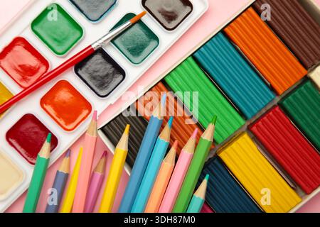 Matite colorate, plasticine e vernici ad acquerello su sfondo rosa. Vista dall'alto Foto Stock