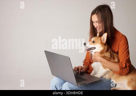 Donna che utilizza un computer portatile con cane corgi che ordina articoli per animali domestici online con spazio per la consegna e-commerce e il concetto digitale di cura degli animali domestici Foto Stock