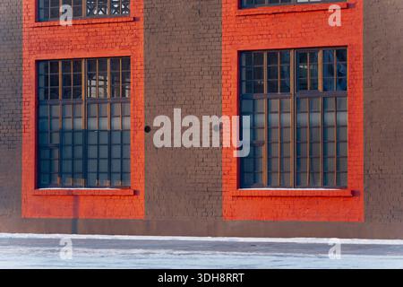 Facciata di un edificio industriale in mattoni con grandi finestre a griglia e neve lungo la base che mostra l'esterno restaurato della fabbrica e dettagli architettonici urbani Foto Stock