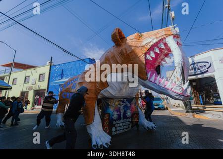 I giovani spingono un grande mâché toro di carta colorato su una cornice a ruote attraverso una piazza soleggiata, con un piccolo cane nelle vicinanze durante un festival in Messico. Foto Stock