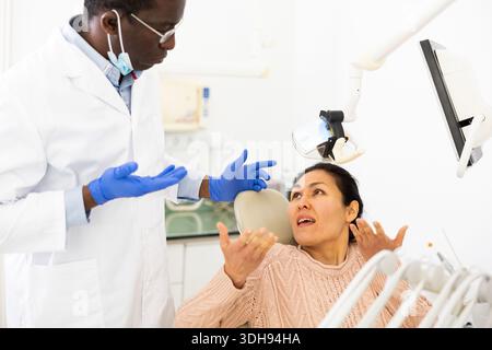 Donna insoddisfatta che parla con un dentista confuso dopo un trattamento dentale Foto Stock
