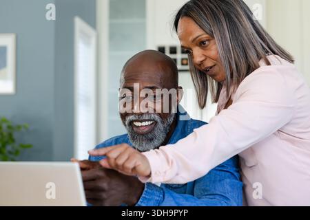 Coppia senior che lavora a casa, uomo afroamericano sorridente e diversificato che punta al laptop Foto Stock