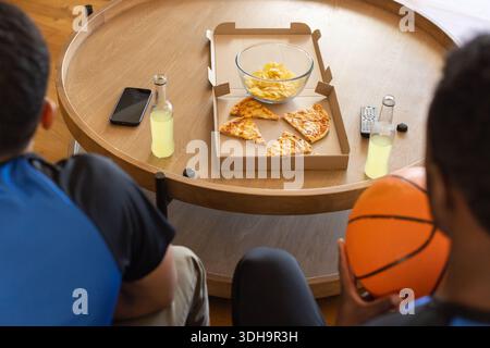 Il tavolino da caffè rotondo in legno contiene pizza, patatine, bottiglie, smartphone e telecomando nel soggiorno Foto Stock