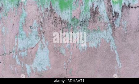 Una parete in cemento resistente agli agenti atmosferici mostra strati testurizzati di vernice rosa e verde, rivelando crepe, muffe e segni di decadimento dovuti all'invecchiamento. Foto Stock