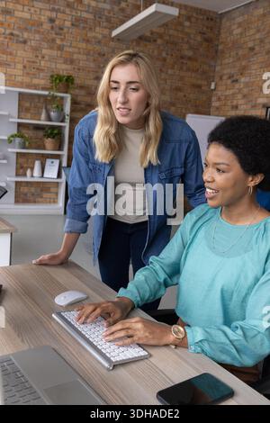 Diverse collaboratrici in denim e tè che collaborano alla scrivania dell'ufficio digitando una sola volta sulla tastiera Foto Stock