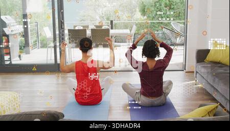 Fare pratica con i partner seduti, alzare le braccia a casa su tappeti blu-viola che indossano abiti da allenamento, HUD Foto Stock