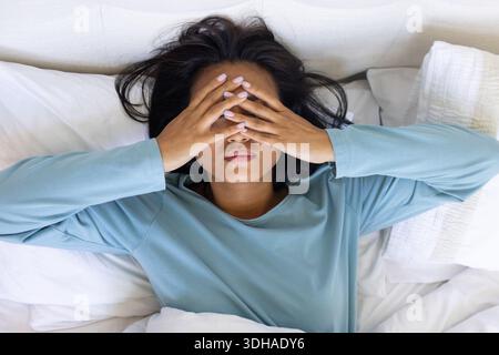 La parte superiore blu a maniche lunghe poggia su un letto bianco con cuscini e testata leggera Foto Stock