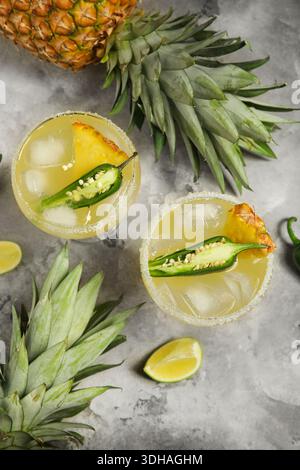 Bicchieri di gustoso cocktail margarita con jalapeno e ananas su sfondo grunge grigio Foto Stock