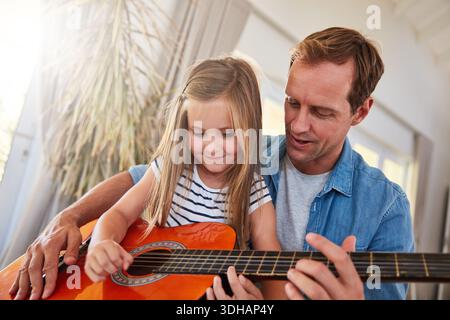 Chitarra, musica e apprendimento con il padre, la ragazza e il legame nel salotto di casa. Strumento, amore e sorriso con genitori, figli e insegnanti Foto Stock