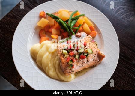 Piatto gourmet di filetto di salmone grigliato con salsa fresca servito insieme a crema di patate, colorate verdure al vapore in un piatto di ceramica Foto Stock