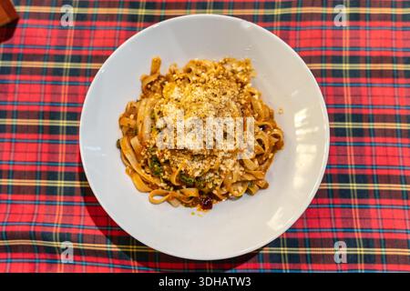 Tagliatelle cotte servite con salsa salata di carne e formaggio in piatto bianco su tovaglia tartan Foto Stock