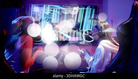 Giocare a due giocatori in berretto, felpa con cappuccio appoggiata nella sala giochi, con monitor, controller e cuffie Foto Stock