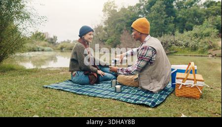 Felice, coppia e picnic con caffè all'aperto per viaggi, bevande calde e avventura di trekking. Sorridi, gente e campeggio con drink a colazione Foto Stock